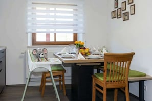 A dining area with a table set for two, a high chair with a stuffed toy, and a window with blinds. - Wohlfühldomizil im Grünen (Leipheim)