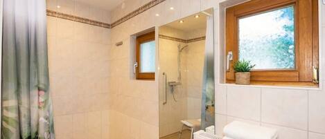 A bathroom with a shower, a toilet, and a window with a plant.