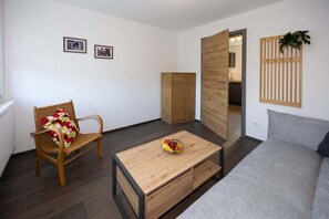 A room with a wooden chair, a small table with a fruit bowl, a grey sofa, a wooden wardrobe, and a wooden door leading to another room. - Wohlfühldomizil im Grünen (Leipheim)