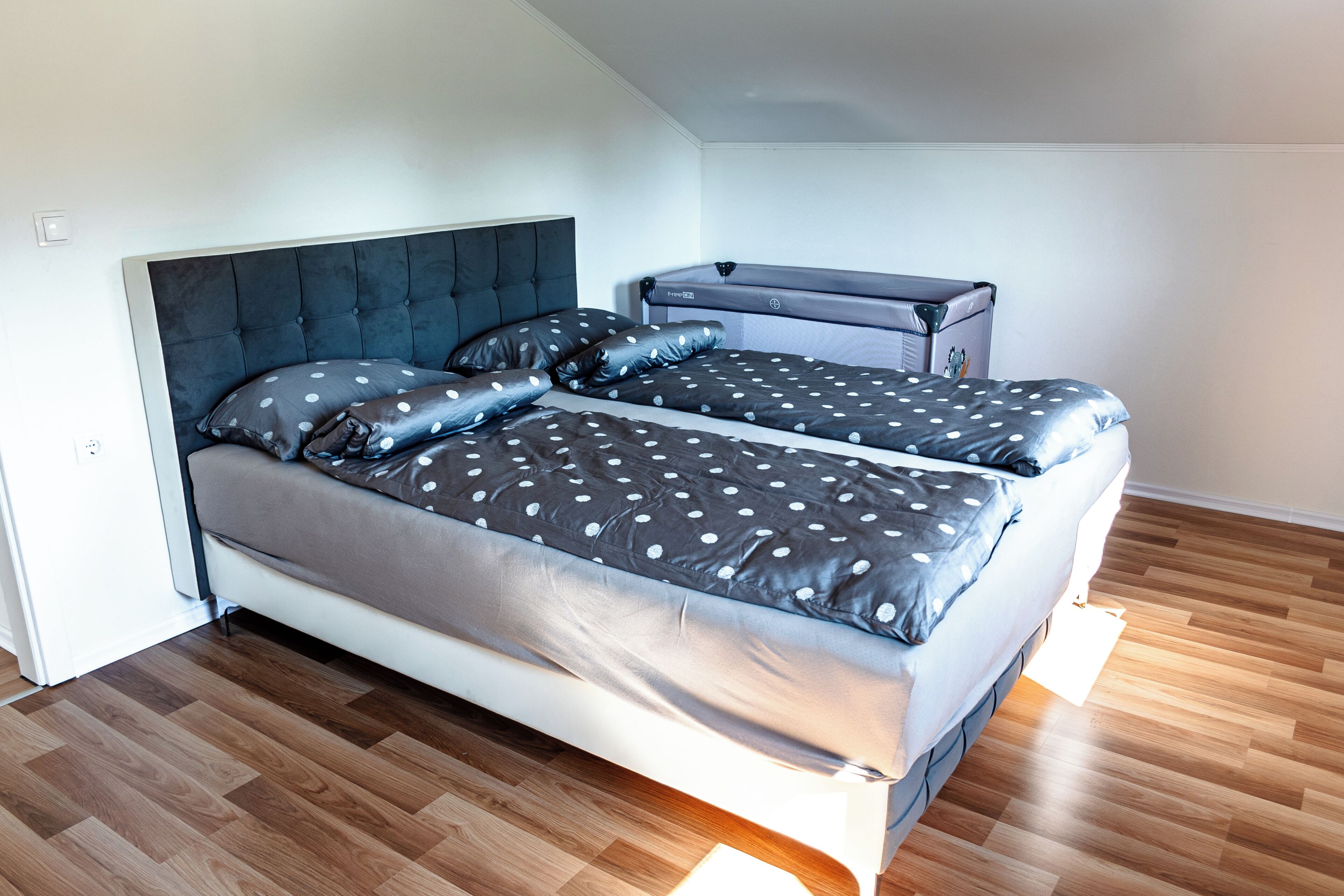 A bedroom with a bed, a chest of drawers, and a wooden floor.