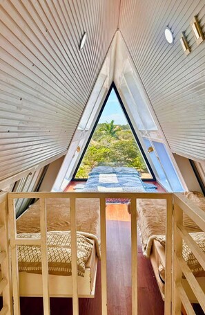 A triangular attic bedroom with a view of a lush landscape.