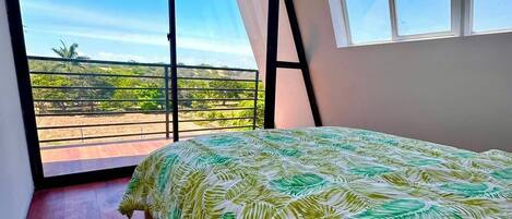 Un dormitorio con una cama grande, vistas del paisaje a través de una ventana y un balcón.
