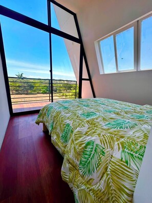 A bedroom with a large bed, a view of the landscape through a window, and a balcony.