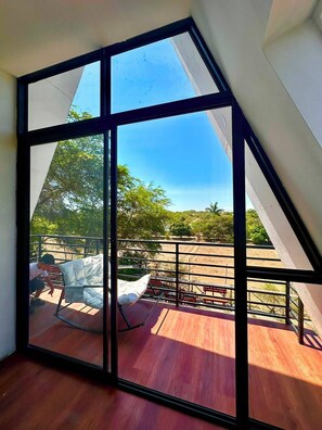 Una habitación con un amplio ventanal, suelo de madera y vistas a un espacio exterior con una silla y una mesa.