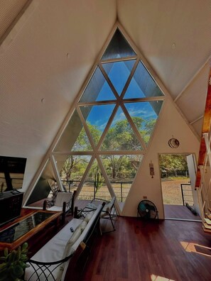A room with a large triangular window, a bed, a desk, and a fan.