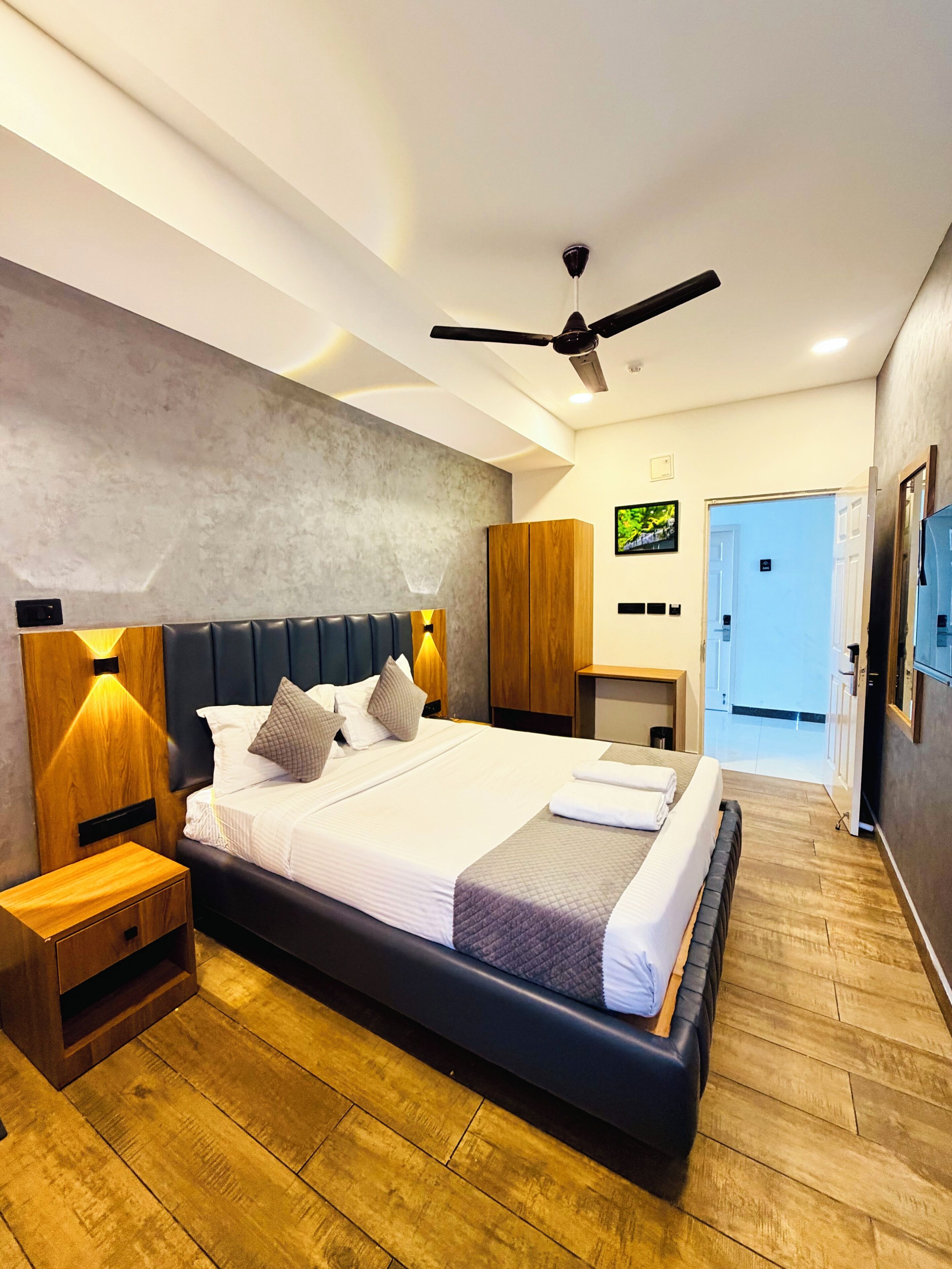 Una habitación de hotel moderna con una cama grande, cabecera de madera y un ventilador de techo.