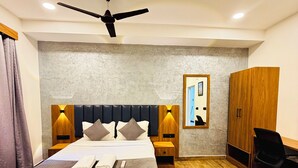 Habitació d'hotel amb un llit, ventilador de sostre, sòl de fusta, armari i escriptori amb cadira.