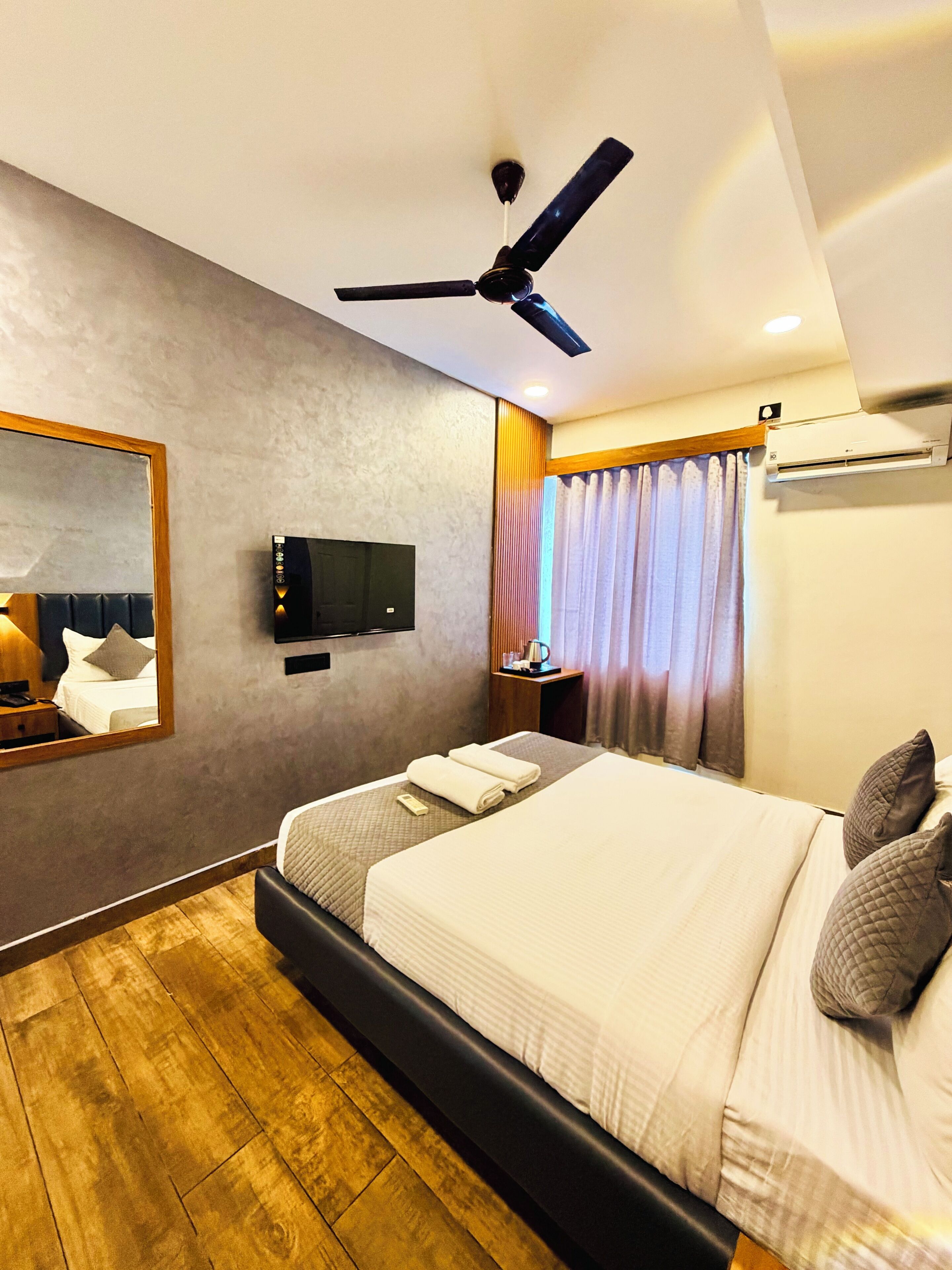 Ein modernes Hotelzimmer mit einem großen Bett, einem Deckenventilator, einem Flachbildfernseher und einem großen Spiegel.