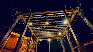 Un área de patio al aire libre con una estructura de pérgola de madera, luces colgantes y varias sillas dispuestas para sentarse.