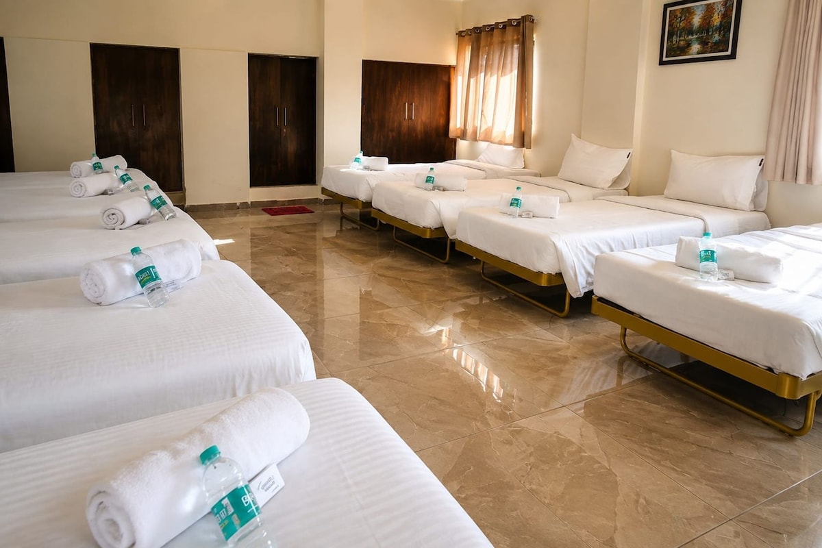 Una habitación de hotel con cuatro camas, cada una con sábanas blancas y una botella de agua.