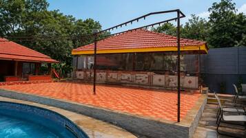A swimming pool with a covered patio area, a children's play structure, and a building with a red-tiled roof.