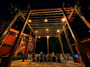 Un patio exterior con una pérgola de madera, luces colgantes y sillas de mimbre.