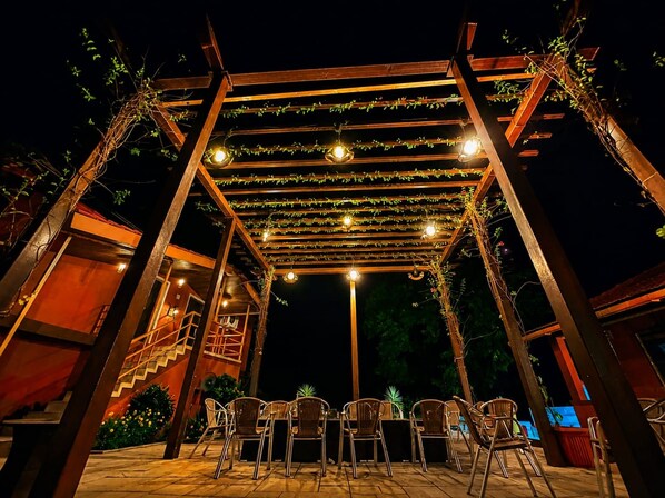An outdoor patio with a wooden pergola, string lights, and wicker chairs.