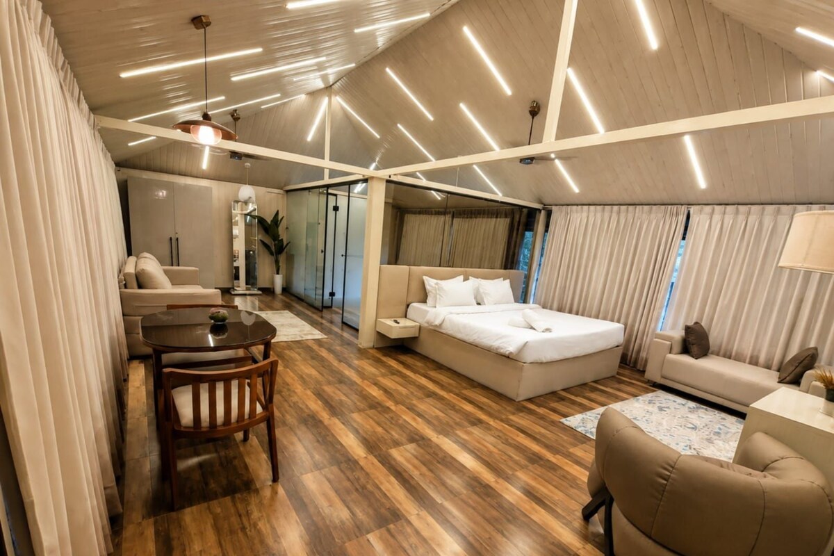 Una habitación de hotel moderna con piso de madera, cama, sofá, mesa de comedor y una mesita con una planta.