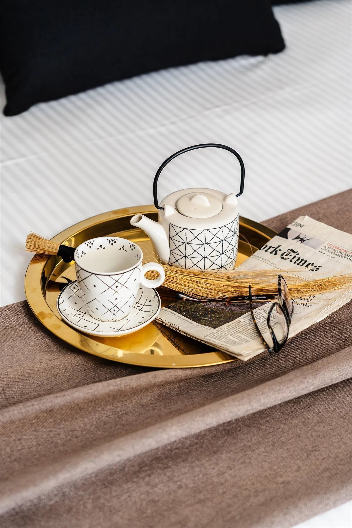 Ein Tablett mit Teekanne, Tassen und einer Zeitung auf einem Bett mit Kissen.