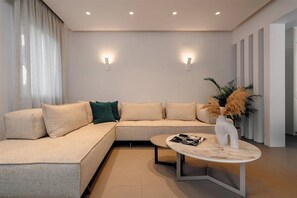 A modern living room with a sectional sofa, a round coffee table, and wall-mounted lighting. - Thalelion 3 Bedroom Villas With Private Pool and Jacuzzi (Naxos)