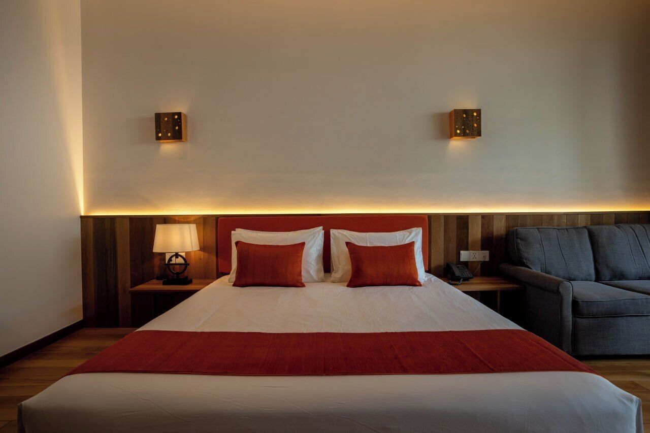 Quarto de hotel com uma cama grande, duas luminárias de cabeceira, um sofá e luminárias fixadas na parede.