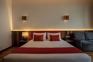 Een hotelkamer met een groot bed, twee bedlampen, een bank en wandlampen.
