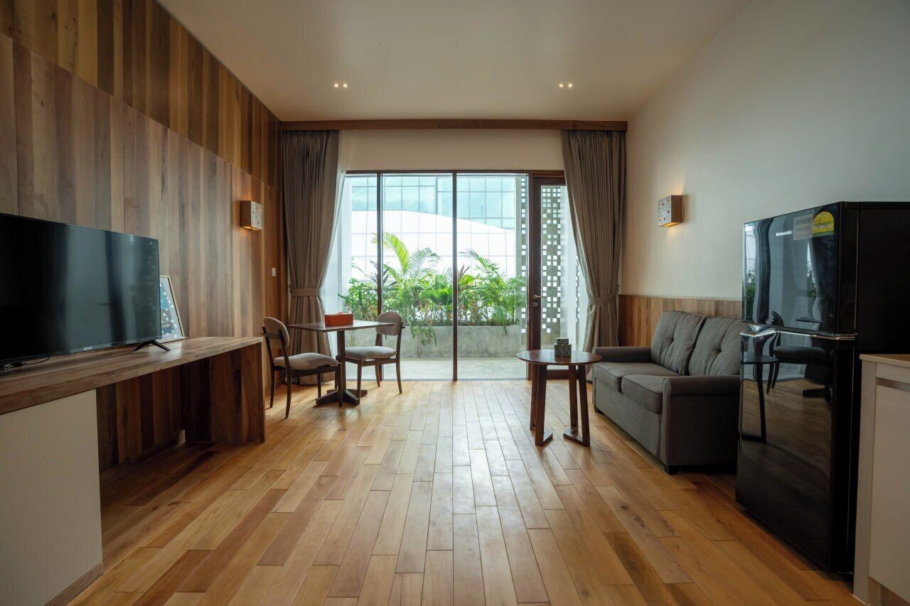 Una sala de estar moderna con una televisión de pantalla plana, piso de madera, un sofá, una mesa de comedor con sillas y un refrigerador.