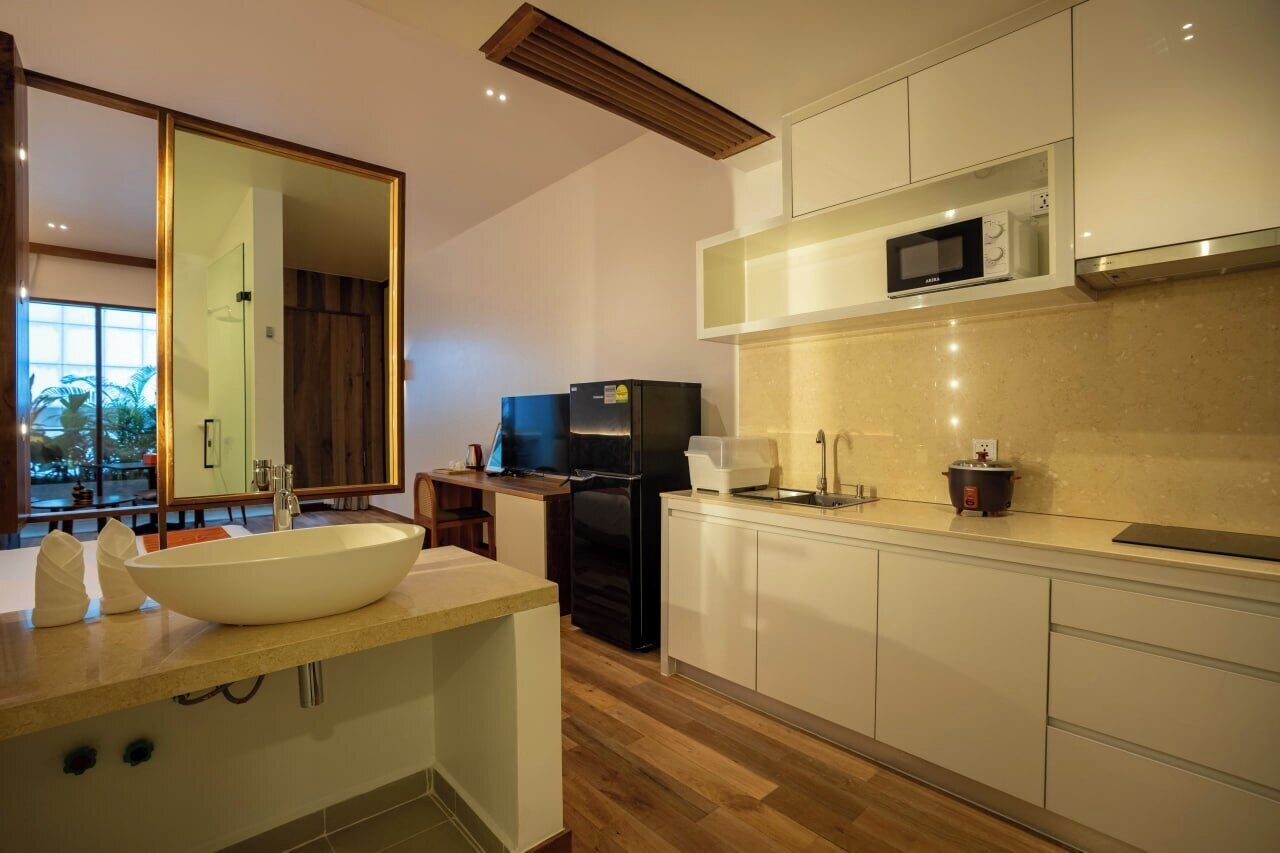 Una cocina moderna con una isla grande, muebles blancos, un microondas y un refrigerador negro.