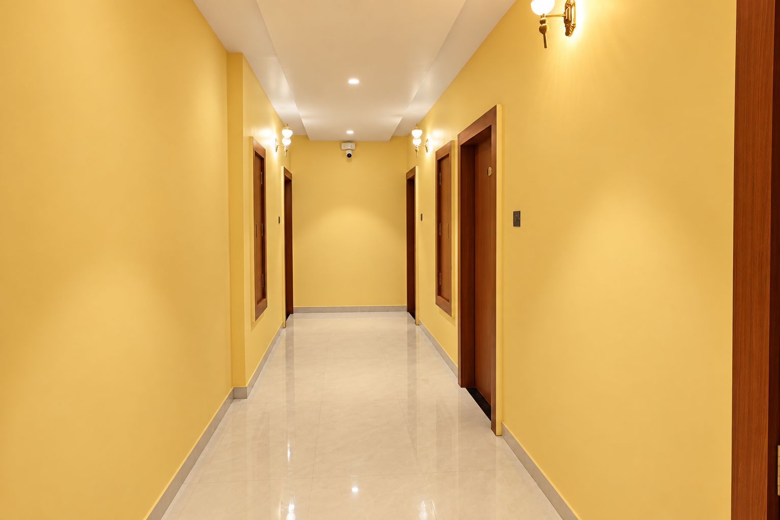 A hotel hallway with a light-colored floor, yellow walls, and doors on both sides.
