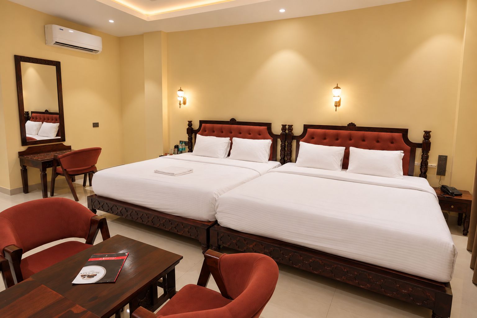 A hotel room with two beds, a desk, chairs, and a mirror.