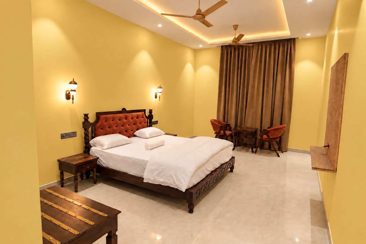 A hotel room with a large bed, two bedside tables, a ceiling fan, and a seating area with two chairs and a table.
