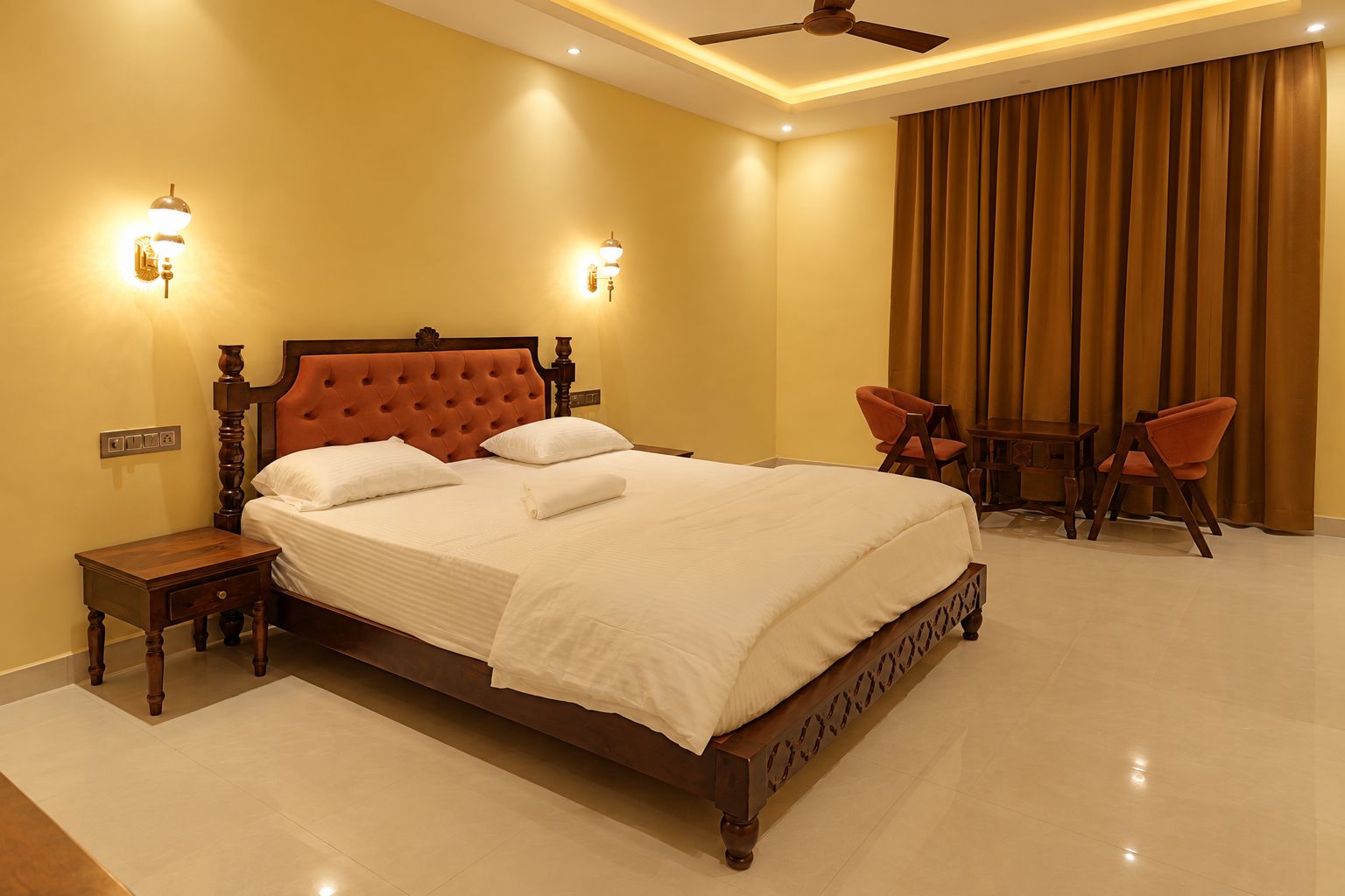 A hotel room with a large bed, two bedside tables, a ceiling fan, and a seating area with two chairs.