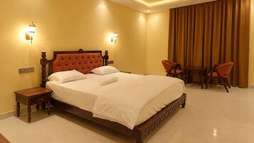A hotel room with a large bed, two bedside tables, a ceiling fan, and a seating area with two chairs.