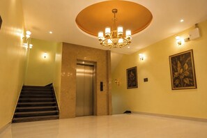 Un vestíbulo de hotel con una escalera, un ascensor, una araña y dos obras de arte enmarcadas en la pared.