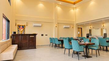 A hotel reception area with a reception desk, a sofa, and a dining area with tables and chairs.