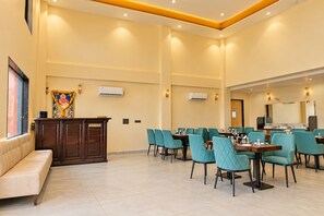 Zona de recepció d'hotel amb taulell de recepció, un sofà i un menjador amb taules i cadires.