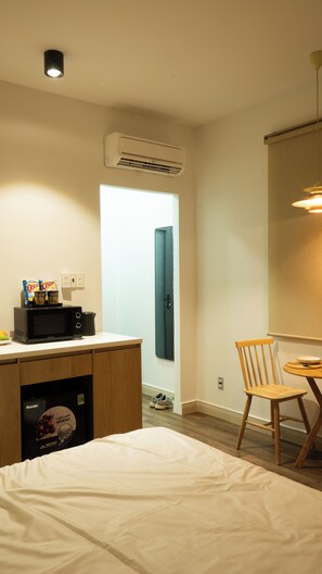 Een hotelkamer met een bed, een magnetron, een tafeltje met een stoel en een airconditioning.