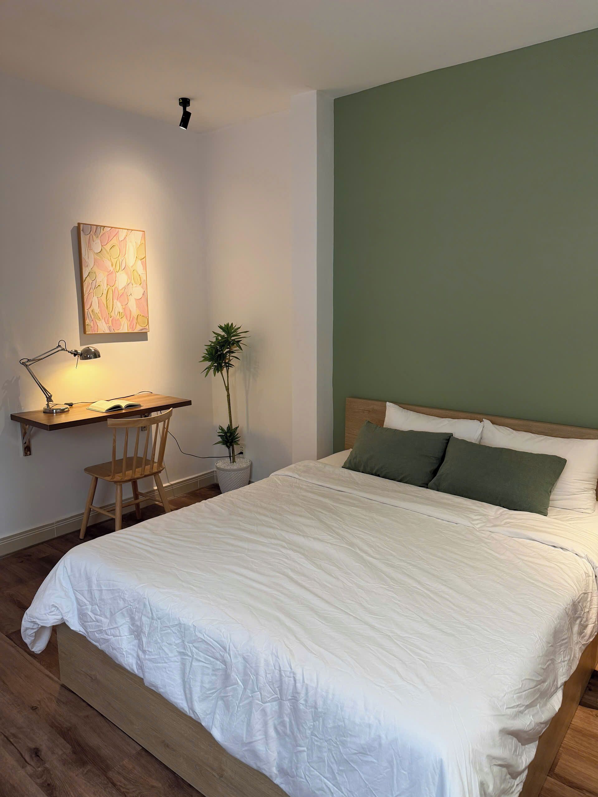 A bedroom with a bed, a desk with a chair, a lamp, and a plant.