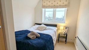 Un dormitorio con cama, mesita de noche, lámpara y ventana con cortina.