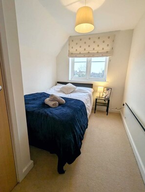 Een slaapkamer met een bed, nachtkastje, lamp en een raam met gordijn.