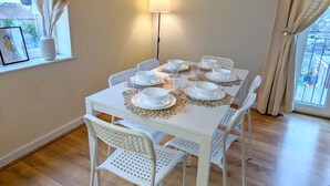 Un comedor con una mesa blanca dispuesta para cuatro, un reloj de pared y una ventana con vistas.