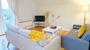 Una sala moderna con un sofá gris, un sillón azul, una mesa de centro blanca y un televisor sobre un mueble.