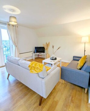 Een moderne woonkamer met een grijze bank, een blauwe fauteuil, een witte salontafel en een televisie op een meubel.