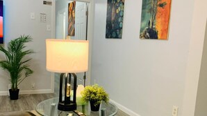 A living room with a glass coffee table, a lamp, a sofa, and two paintings on the wall.