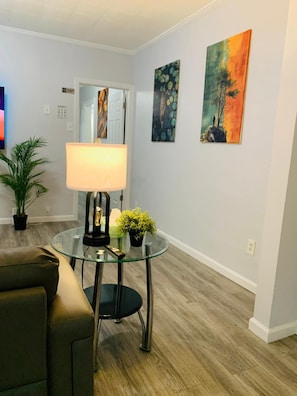 A living room with a glass coffee table, a lamp, a sofa, and two paintings on the wall.