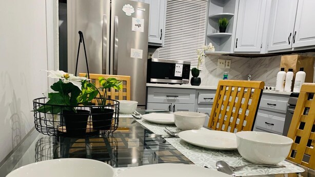 A modern kitchen with stainless steel appliances, a dining table set with white plates and bowls, and a potted plant on the table.