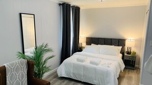 A hotel room with a large bed, two bedside tables with lamps, a potted plant, and a brown leather chair.
