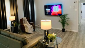 A modern living room with a flat-screen TV, a sofa, two side tables with lamps, and a potted plant.
