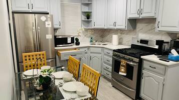 A modern kitchen with white cabinetry, stainless steel appliances, and a dining area with a glass table and chairs.