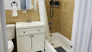 A bathroom with a white sink, mirror, and cabinet, a shower with a handheld showerhead, and a bathtub with a shower curtain.