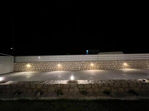 Eine Steinterrasse mit integrierter Beleuchtung, ein weißer Zaun und eine Steinmauer.