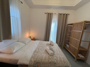 Ett hotellrum med en säng, en garderob i trä och ett nattduksbord med en lampa.