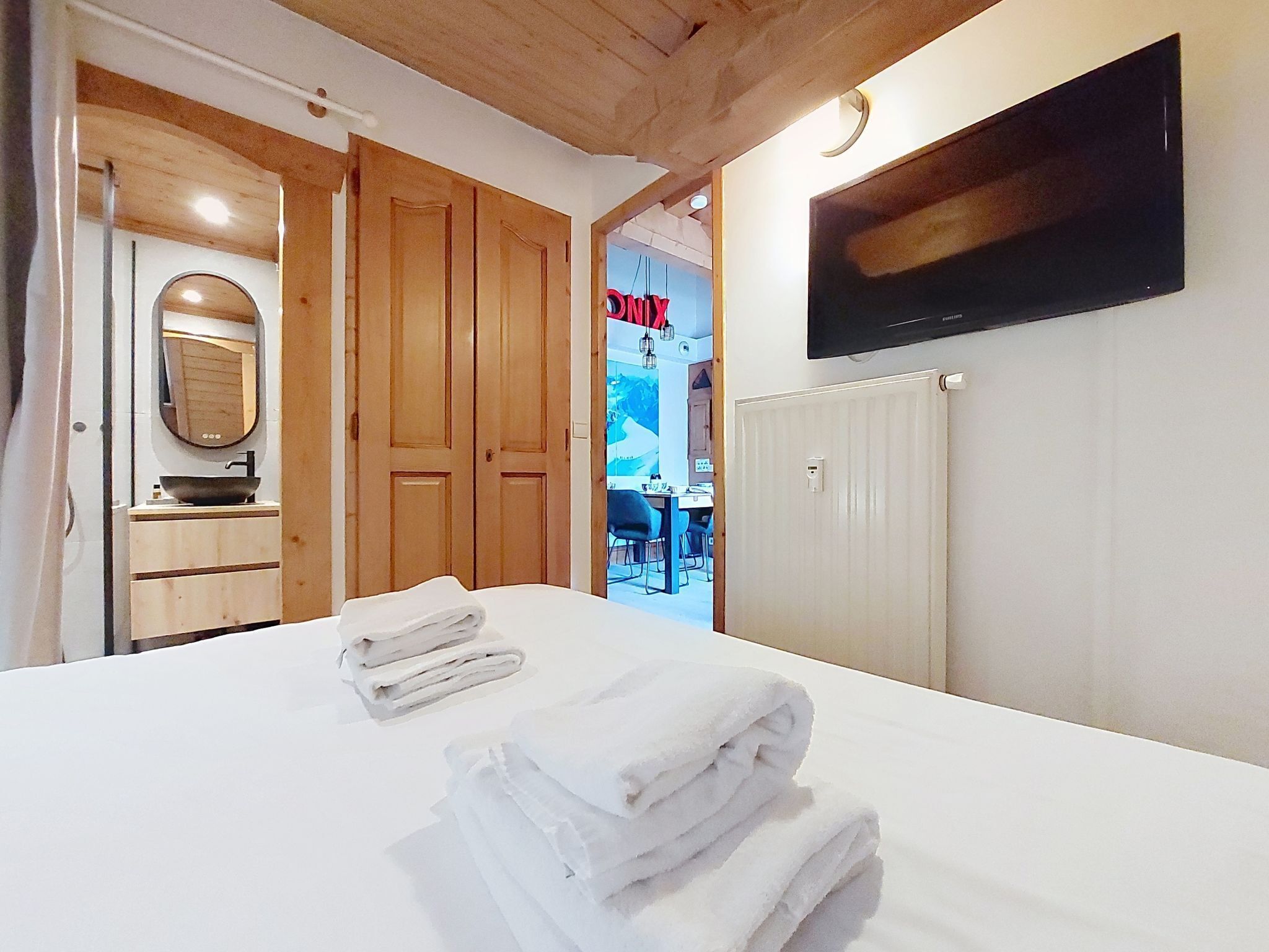 A hotel room with a bed, a mirror, a TV, and wooden doors.
