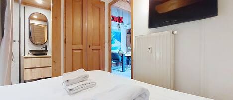 Una habitación de hotel con cama, espejo, televisor y puertas de madera.